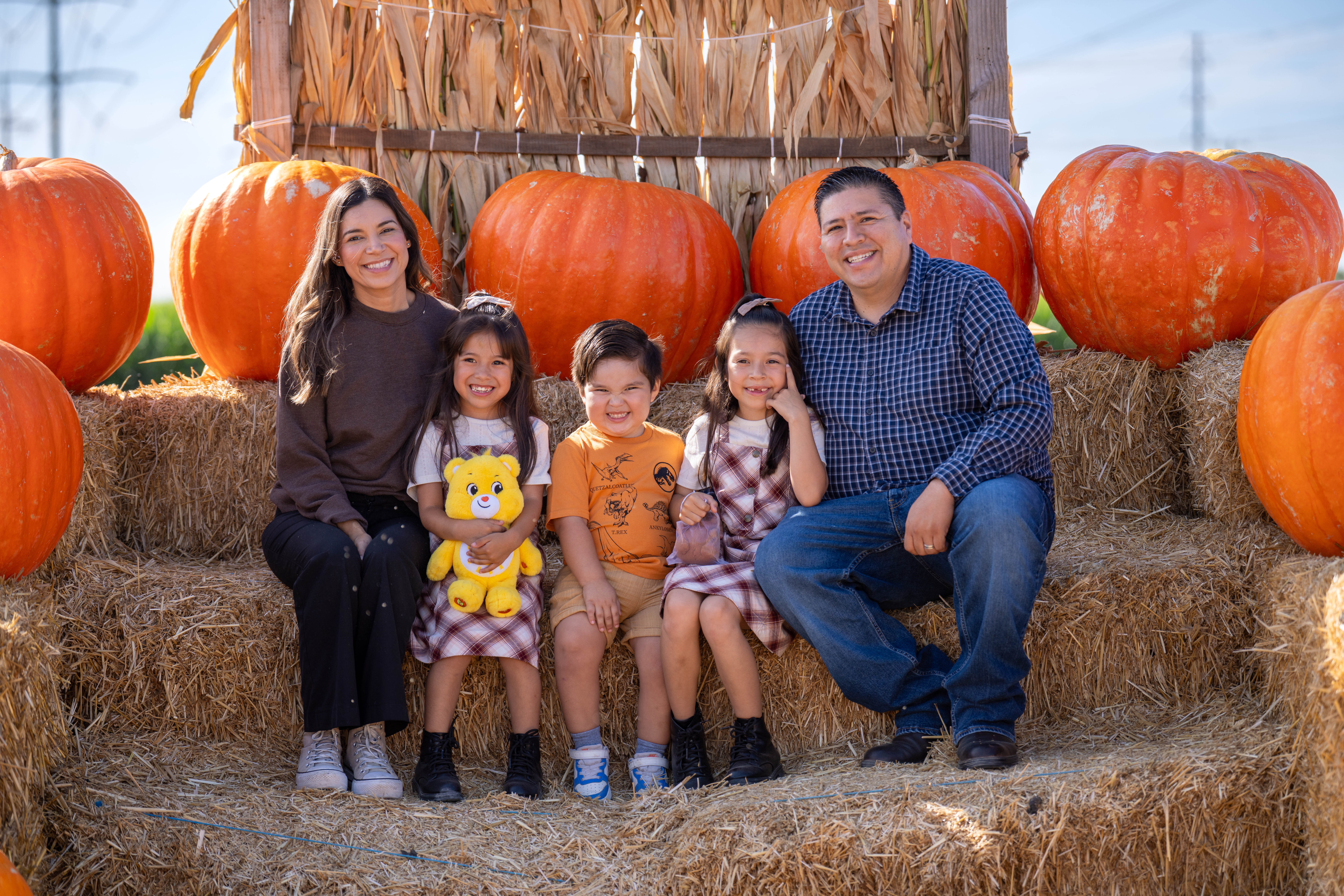 Family of five sitting together on hay bales surrounded by pumpkins