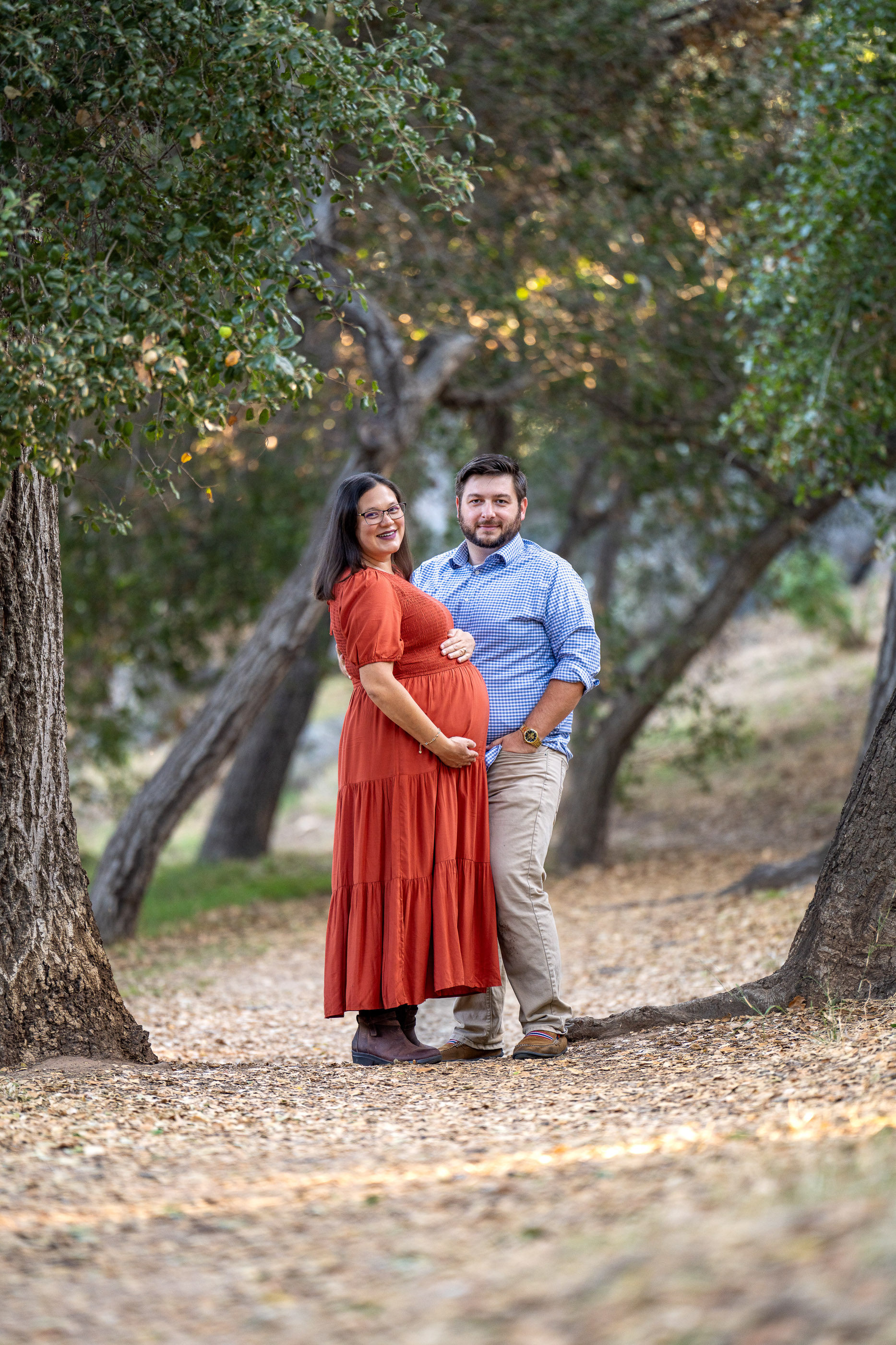 Expecting couple standing together beneath trees during an outdoor maternity session